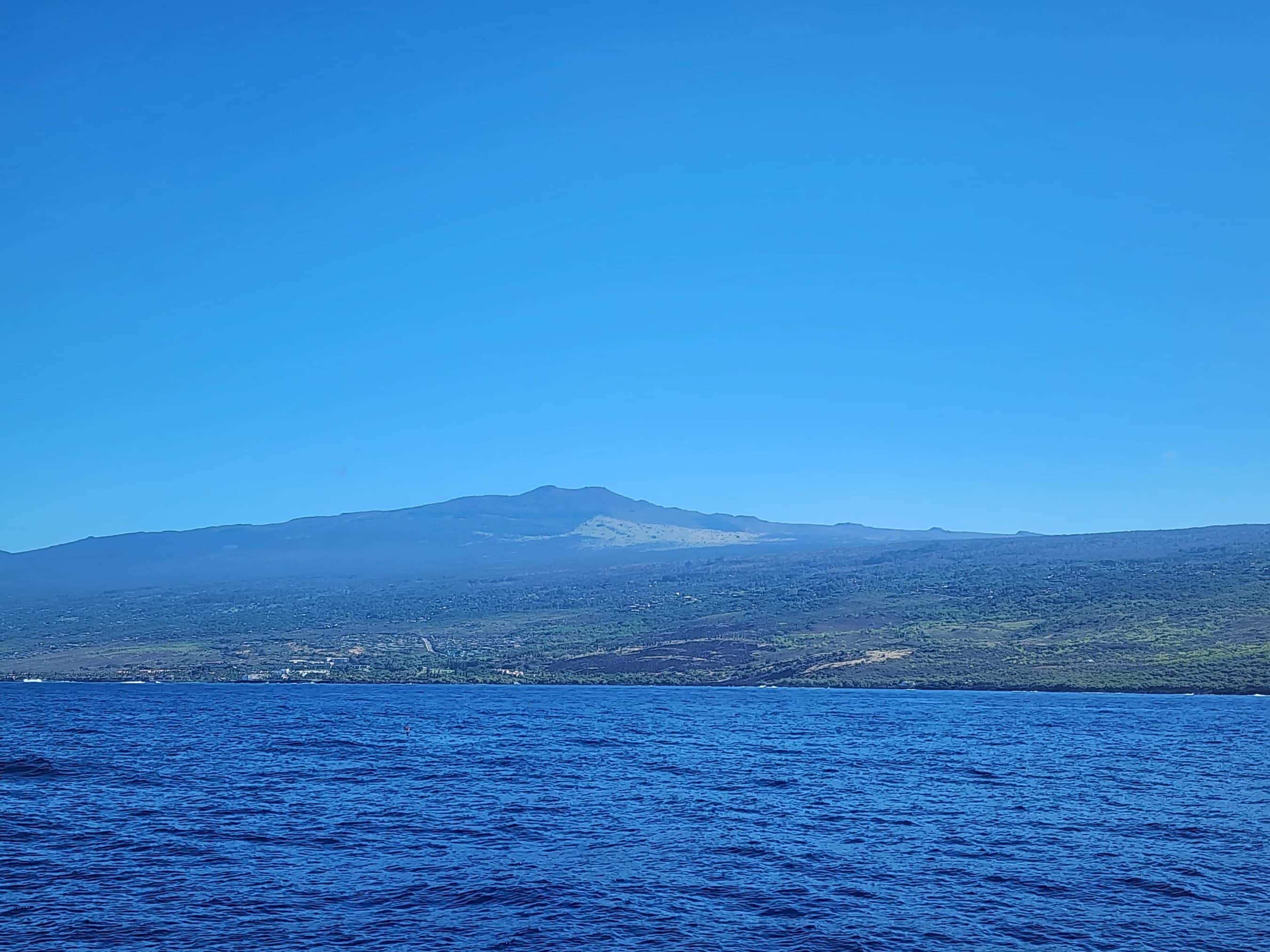 Wide view of a dark blue ocean meeting a distant range of hills under a clear blue sky on a bright day.
