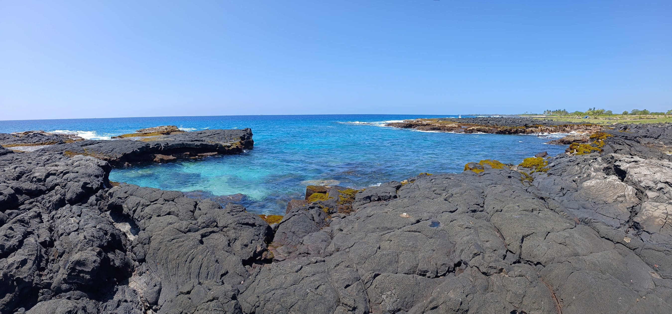 Rocky lava coastline with turquoise water and a clear blue sky on a sunny day near the coast.