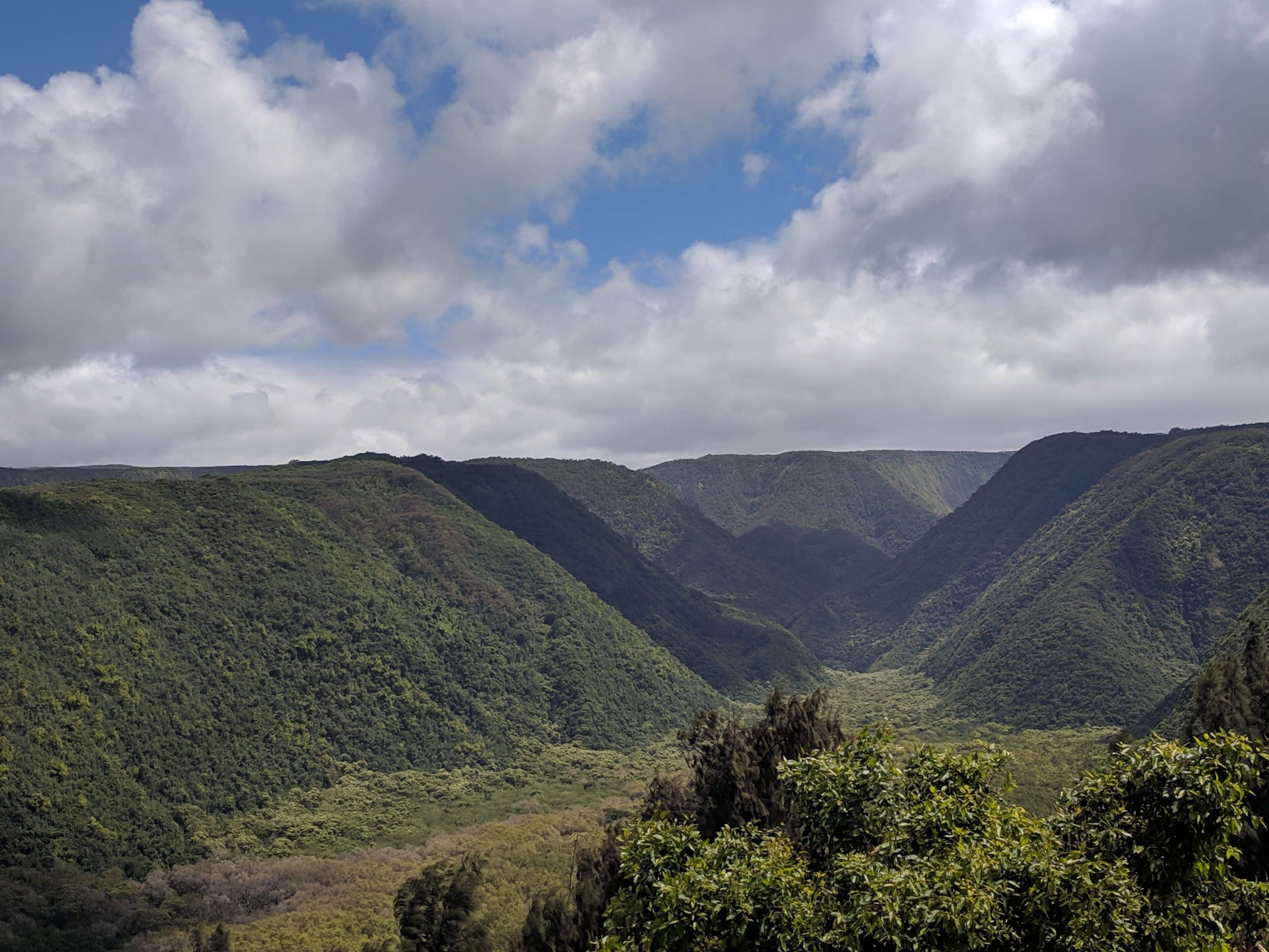 Wide valley with green forested hills and a cloudy sky above mountain ridges.