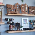 Display of colorful beaded bracelets on wooden stands with a necklace on a black bust and a small plant nearby in a jewelry shop window interior.